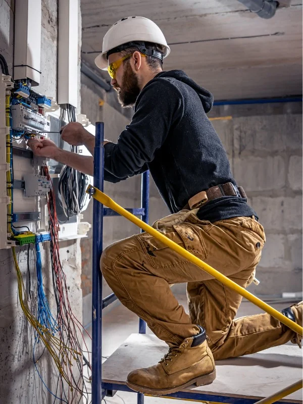 Ein Mann mit Bart arbeitet als Elektriker an einem Schaltkasten